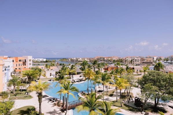 Resort com piscina rodeada por palmeiras e vista para o oceano.