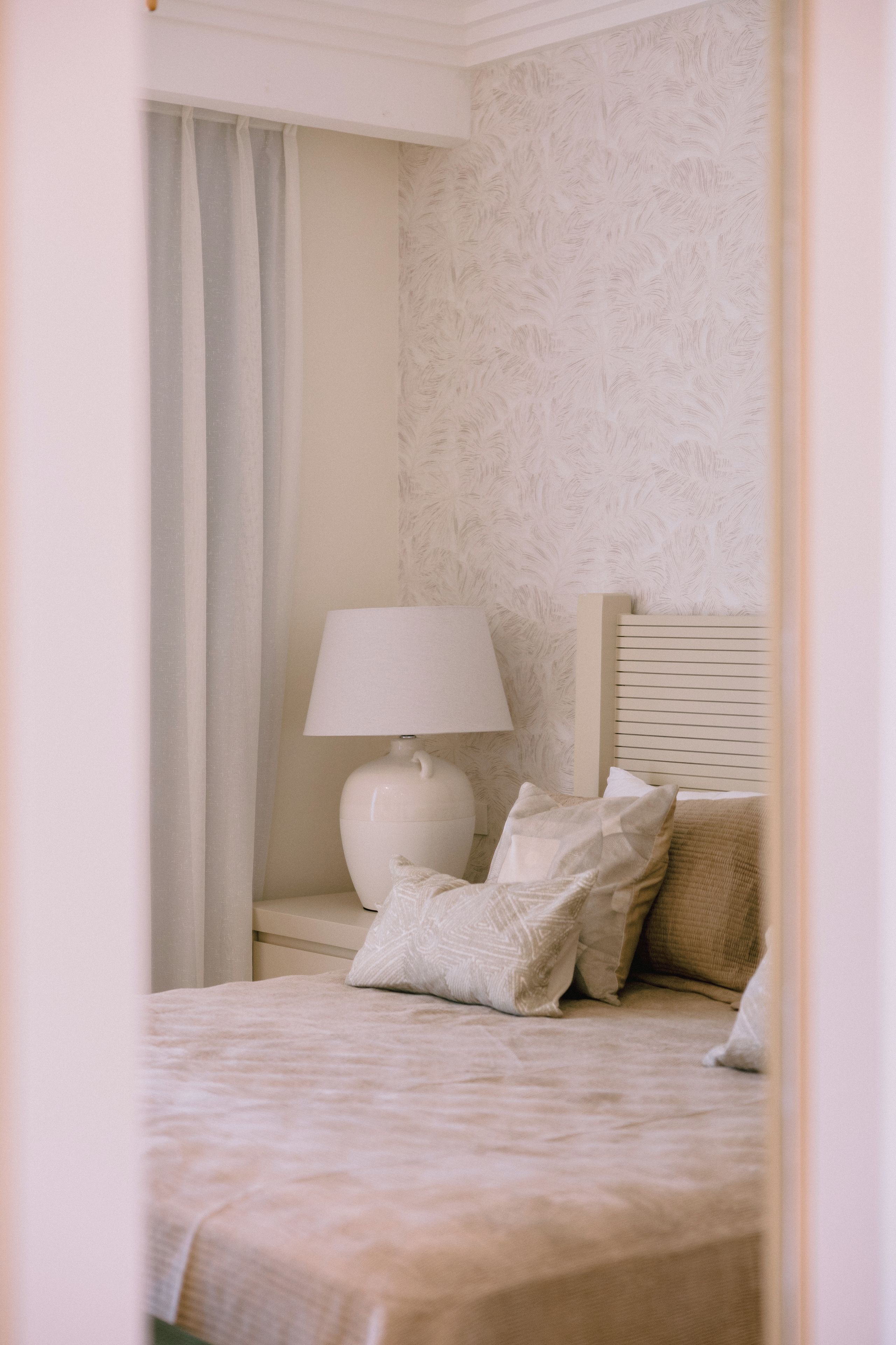 Een slaapkamer met een bed, nachtkastje, lamp en een raam met gordijnen.