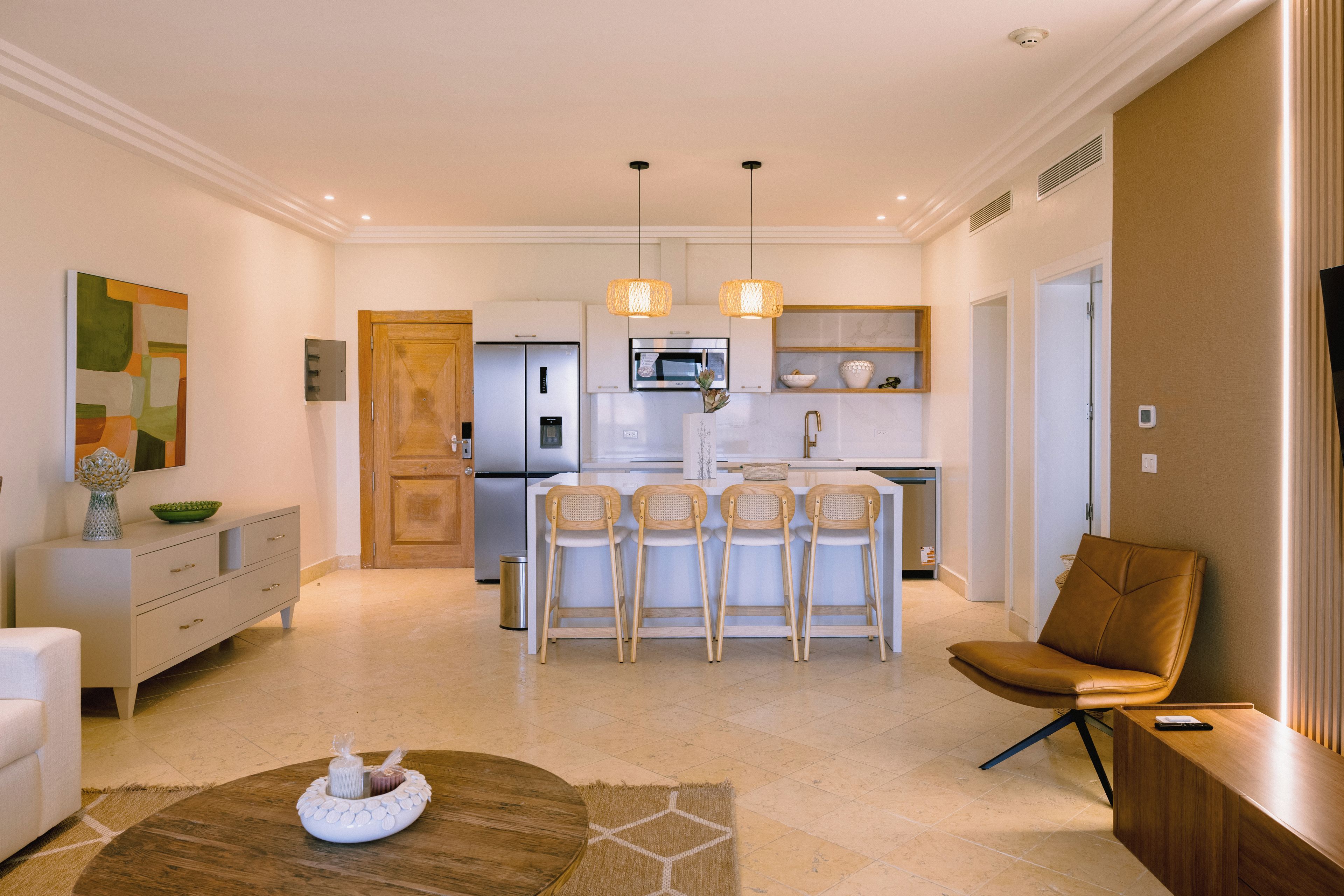 A modern kitchen with a central island, bar stools, and a dining area with a brown leather chair.