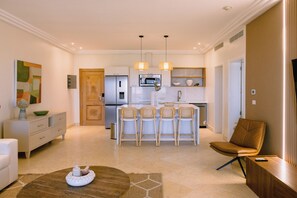 A modern kitchen with a central island, bar stools, and a dining area with a brown leather chair. - Marina View 2BR Apartment  Cap Cana (Punta Cana)