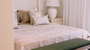 A bedroom with a bed, a bedside table with a lamp, a bench, and a window with curtains. - Marina View 2BR Apartment  Cap Cana (Punta Cana)