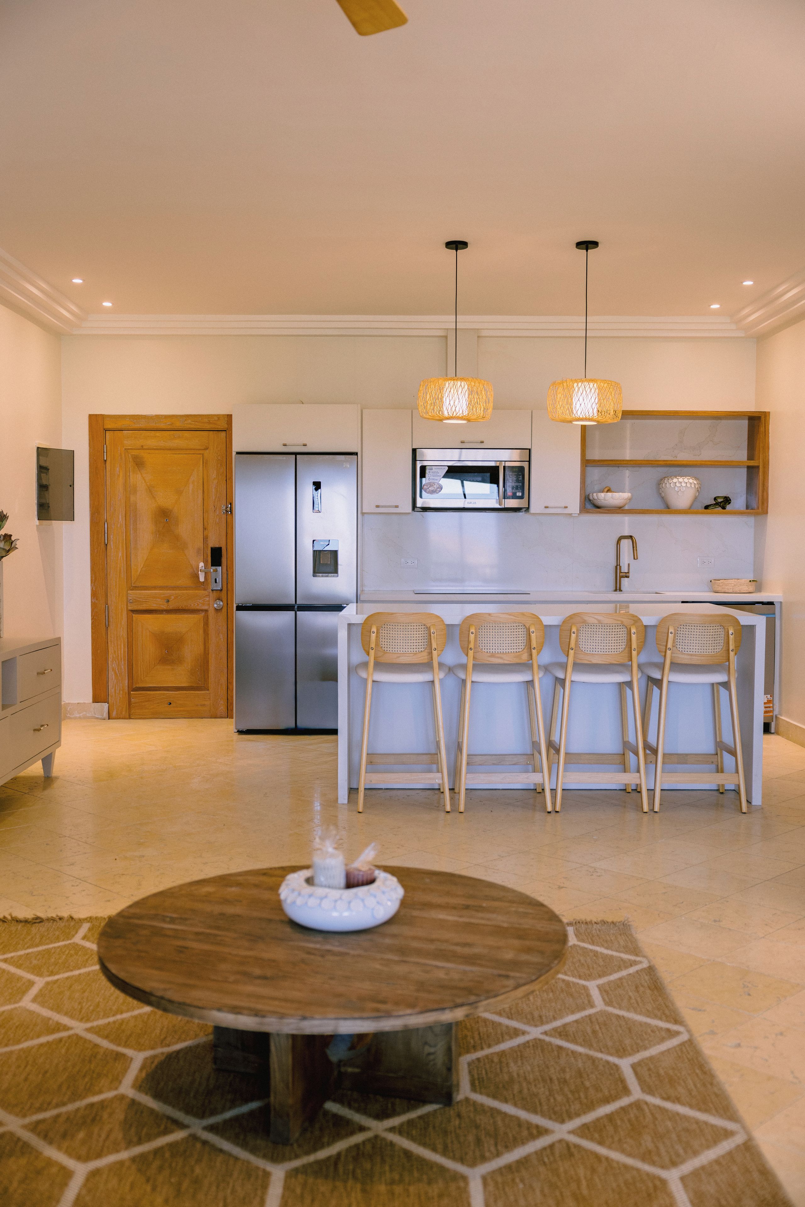 Una cocina moderna con microondas integrado, refrigerador y sillas de madera en una barra.