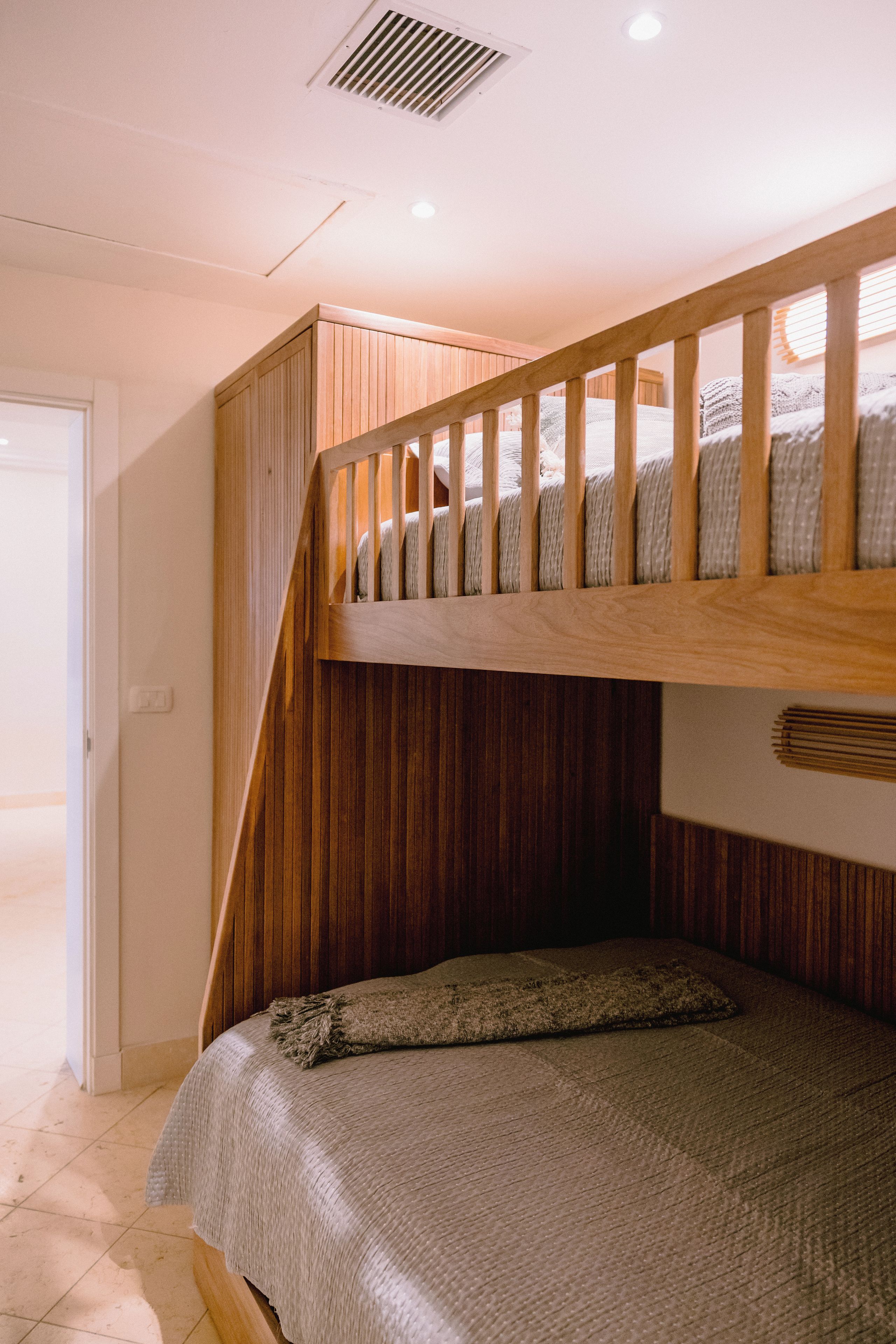 A bunk bed with a wooden ladder and a headboard, a door to the left, and a light fixture on the ceiling.