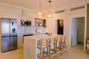 A modern kitchen with stainless steel appliances, a central island with bar stools, pendant lighting, and a view into the adjacent dining area.
