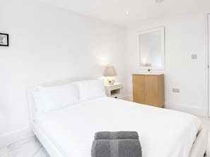 A bedroom with a large bed, a bedside table with a lamp, a wooden wardrobe, and a mirror on the wall. - Spacious Garden Retreat w/ Free Parking Near Canterbury (Canterbury)