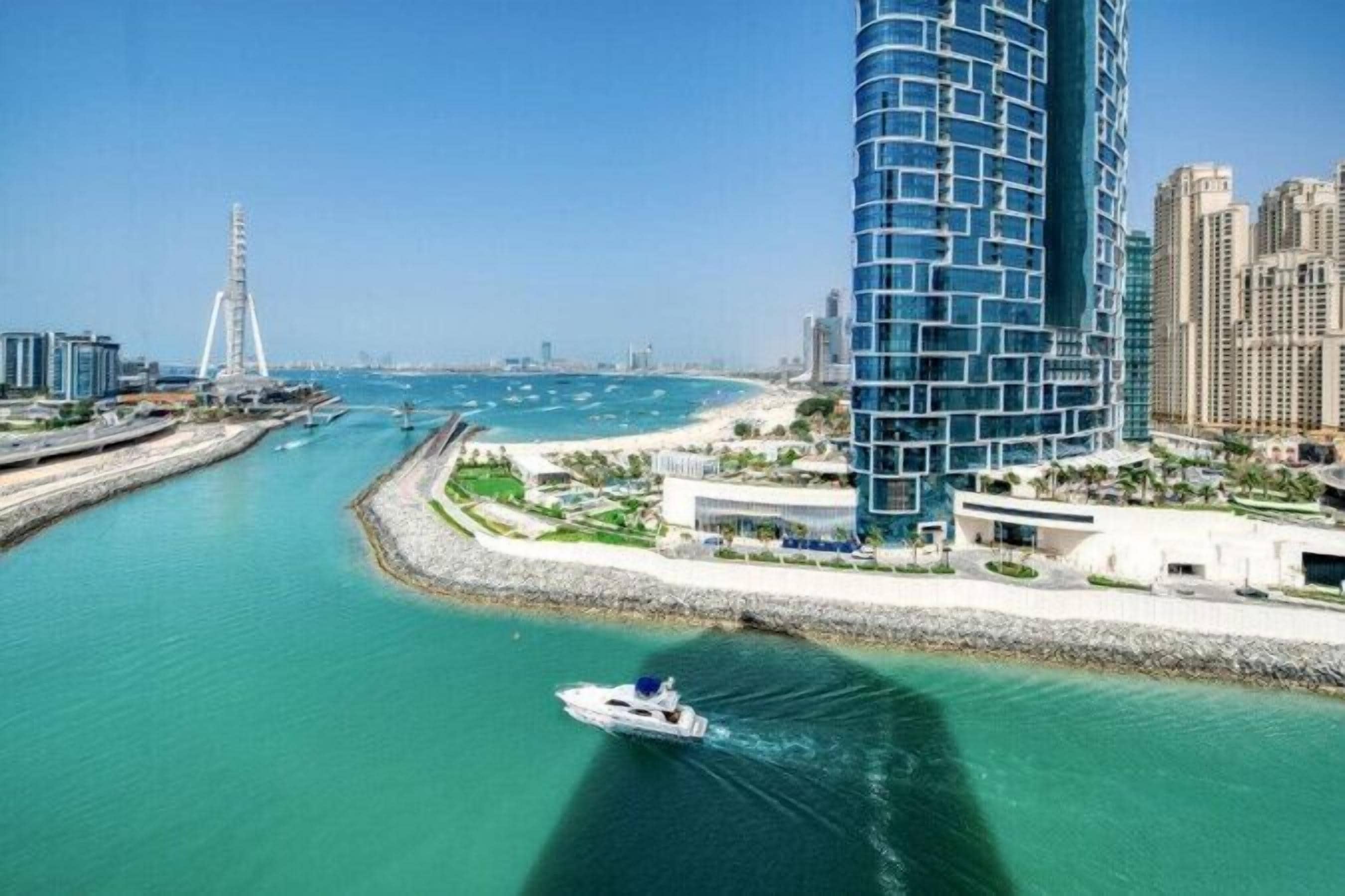 Paisatge urbà costaner amb un edifici modern destacat, una marina i un pont al fons.