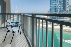 A balcony with a glass table and chairs, overlooking a beach and a tall building. - 52 42 Tower 1 (Dubai)