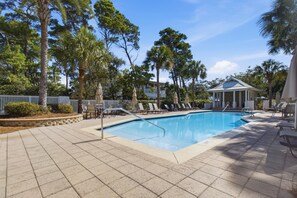 A swimming pool with lounge chairs and umbrellas, surrounded by trees and a building with a covered area. - Sunshine & Tailwinds (Santa Rosa Beach)