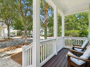A covered porch with white railings, a brick pathway, and a row of chairs. - Sunshine & Tailwinds (Santa Rosa Beach)