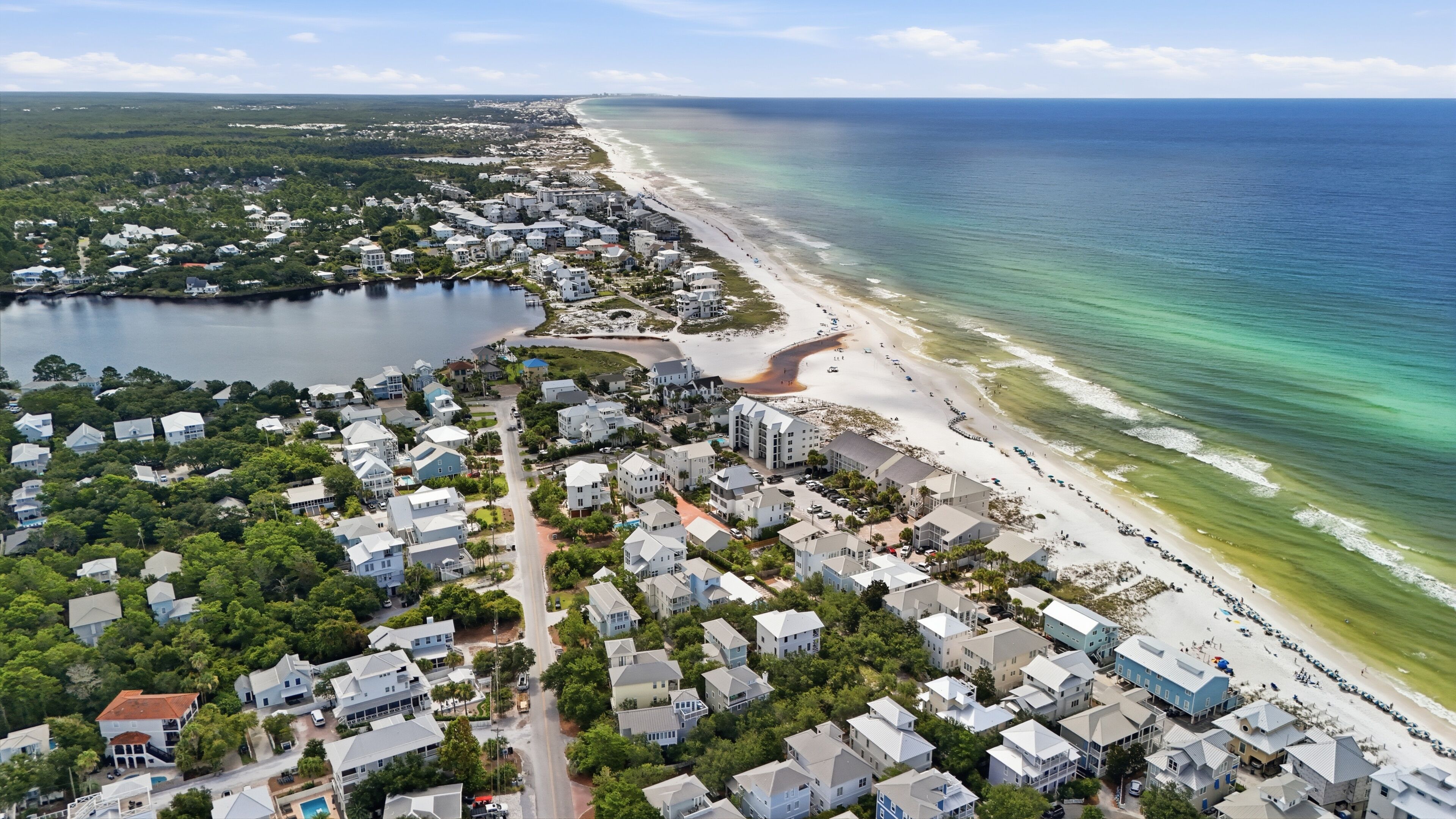 An aerial view of a coastal residential area with houses, a beach, and a body of water.