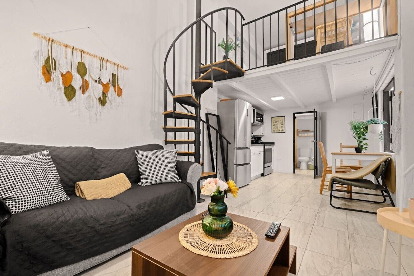 Ein moderner Wohnraum mit einem schwarzen Sofa, einem Holztisch, einer Wendeltreppe und einer Küchenzeile.