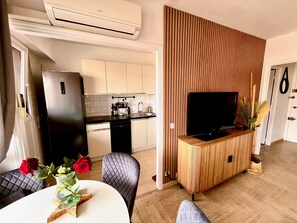 A modern kitchen with a refrigerator, stove, and sink. There is a dining area with a table and chairs, and a television on a wooden cabinet. - Riviera Suite Apartment for 3–4 people, a 12-minute walk from the Cannes Train Station (Cannes)