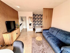A modern living room with a flat-screen TV, a blue sofa, a wooden cabinet, and a patterned wall. - Riviera Suite Apartment for 3–4 people, a 12-minute walk from the Cannes Train Station (Cannes)
