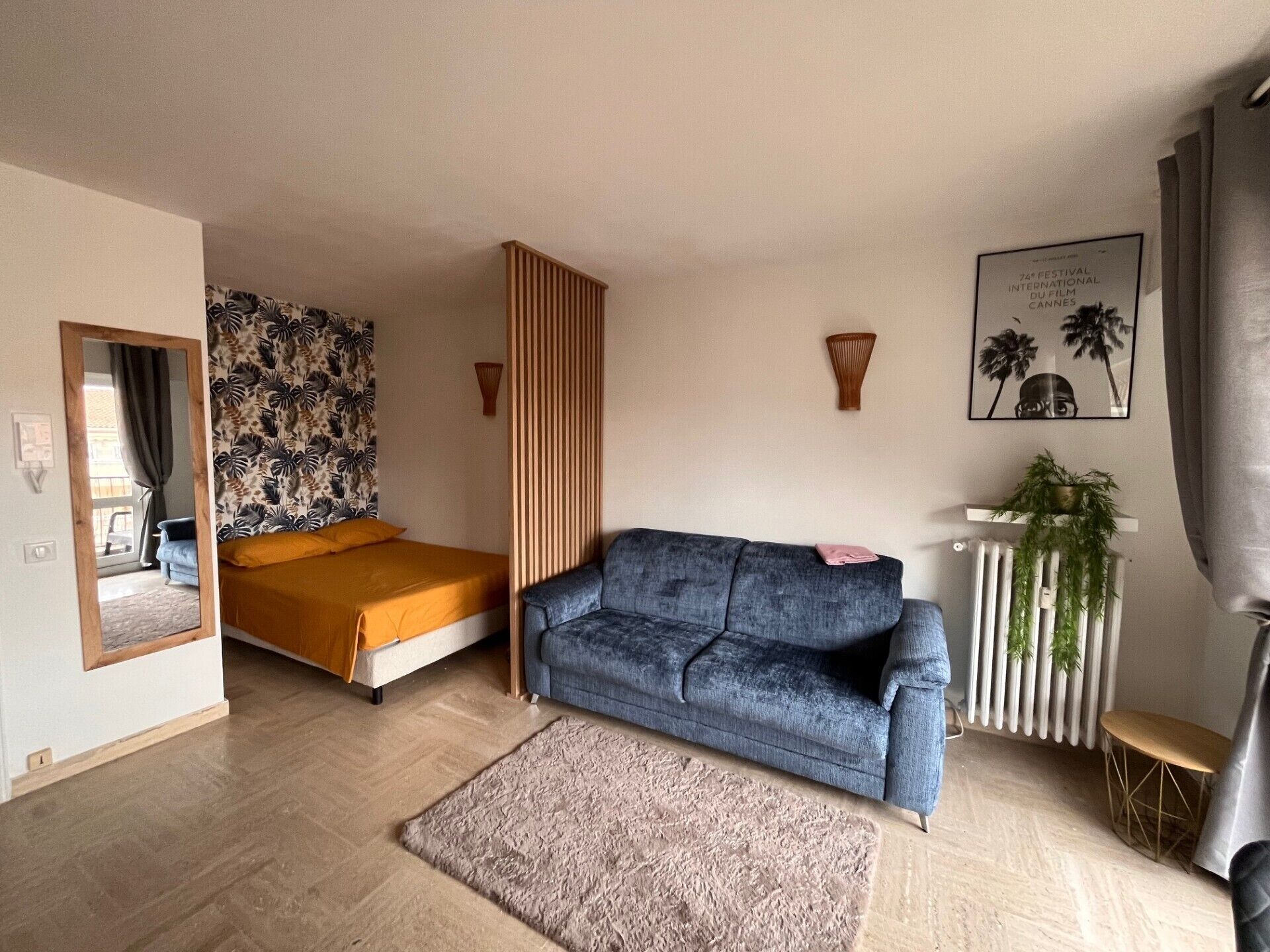 A modern living room with a bed, a sofa, a radiator, and a framed picture on the wall.