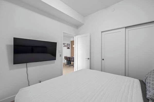 Un dormitorio con una cama, un televisor montado en la pared y una puerta que da al baño.