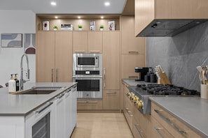 A modern kitchen with built-in appliances, a stainless steel sink, and wooden cabinetry. - Beachside Stay in Kelowna | Pool, Gym & Sauna (Kelowna)