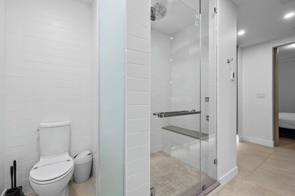 A modern bathroom with a toilet, a glass-enclosed shower, and a visible trash bin.