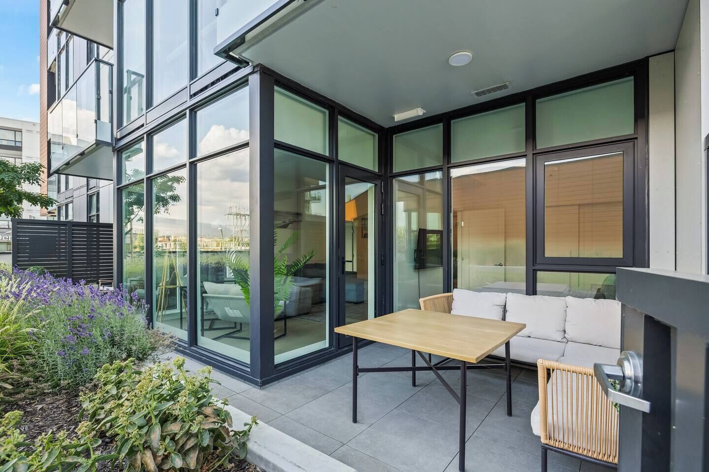 A modern outdoor patio with a glass enclosure, a wooden table, and a white sofa.