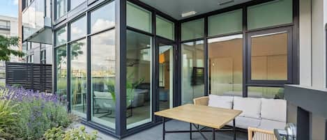 Une terrasse extérieure moderne, dotée d’une véranda en verre, d’une table en bois et d’un canapé blanc.