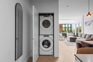 A modern laundry room with two stacked front-loading washers and dryers, a wooden floor, and a view of an outdoor patio with seating.