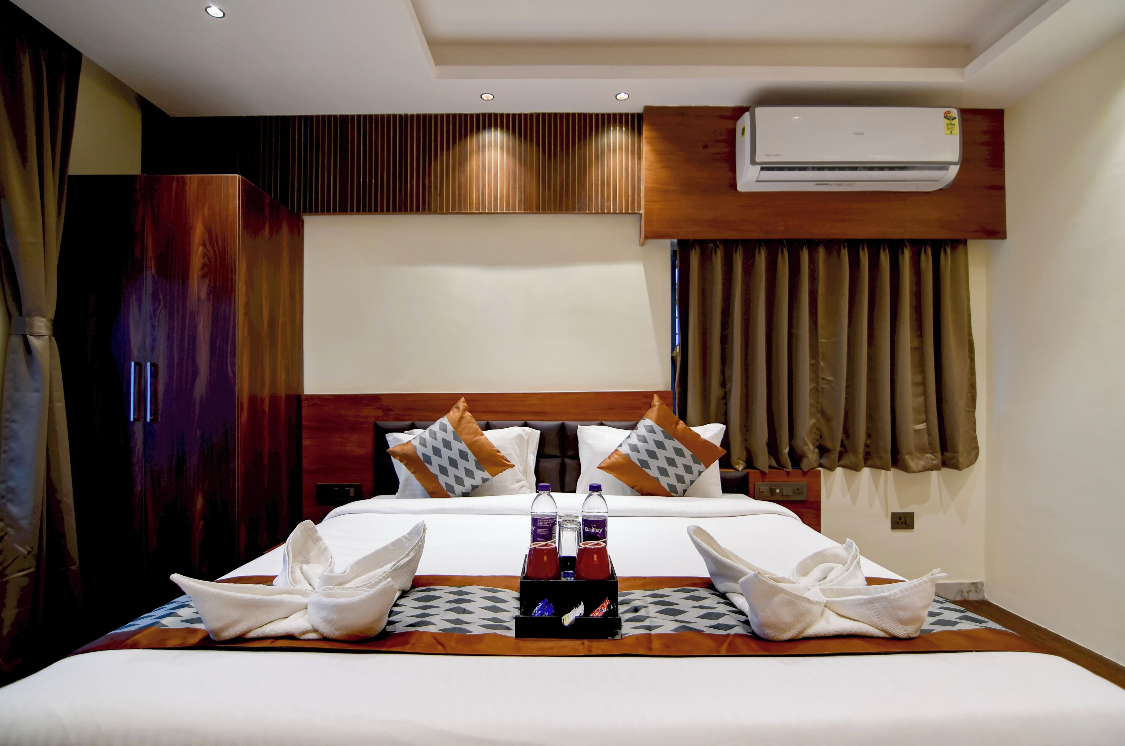 A hotel room with a bed, pillows, a water bottle, a bottle of hand sanitizer, and towels.