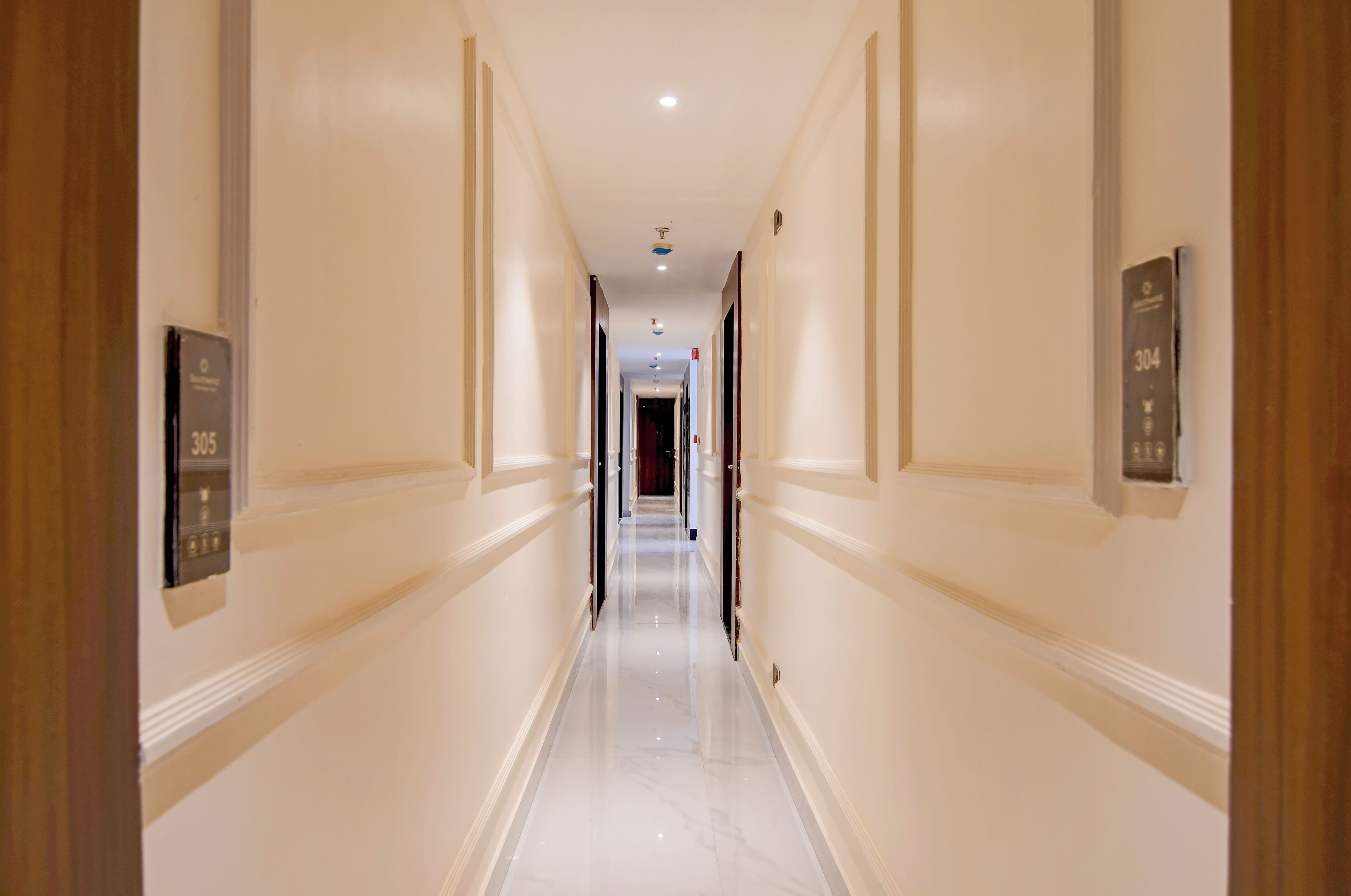 Un pasillo de hotel con piso pulido, paredes blancas y puertas con los números 304 y 305.
