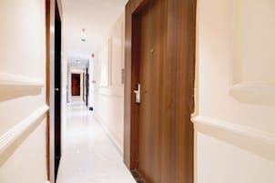 Un pasillo de hotel con una puerta de madera, paredes blancas y suelo de mármol.
