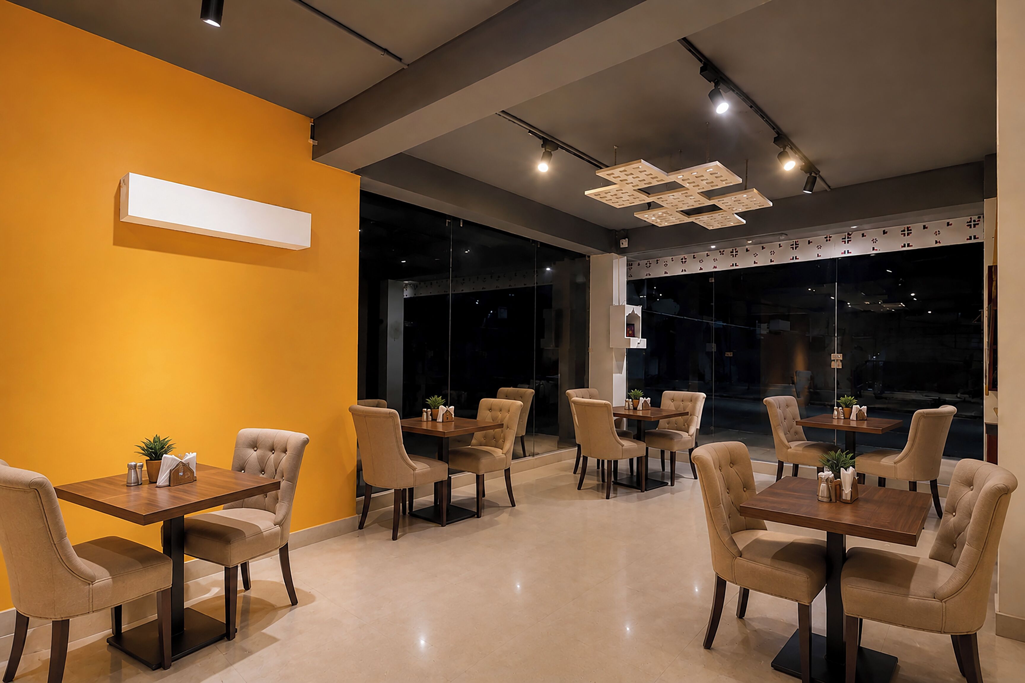 A modern dining area with multiple tables and chairs, a bright yellow accent wall, and a contemporary ceiling design.
