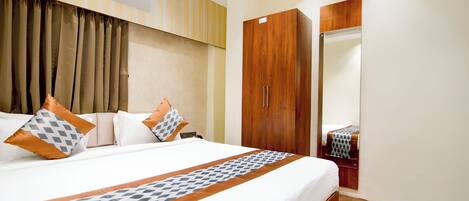 A hotel room with a large bed, a wardrobe, a mirror, and an air conditioning unit.
