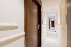 A hotel corridor with a wooden door, white walls, and a shiny floor.