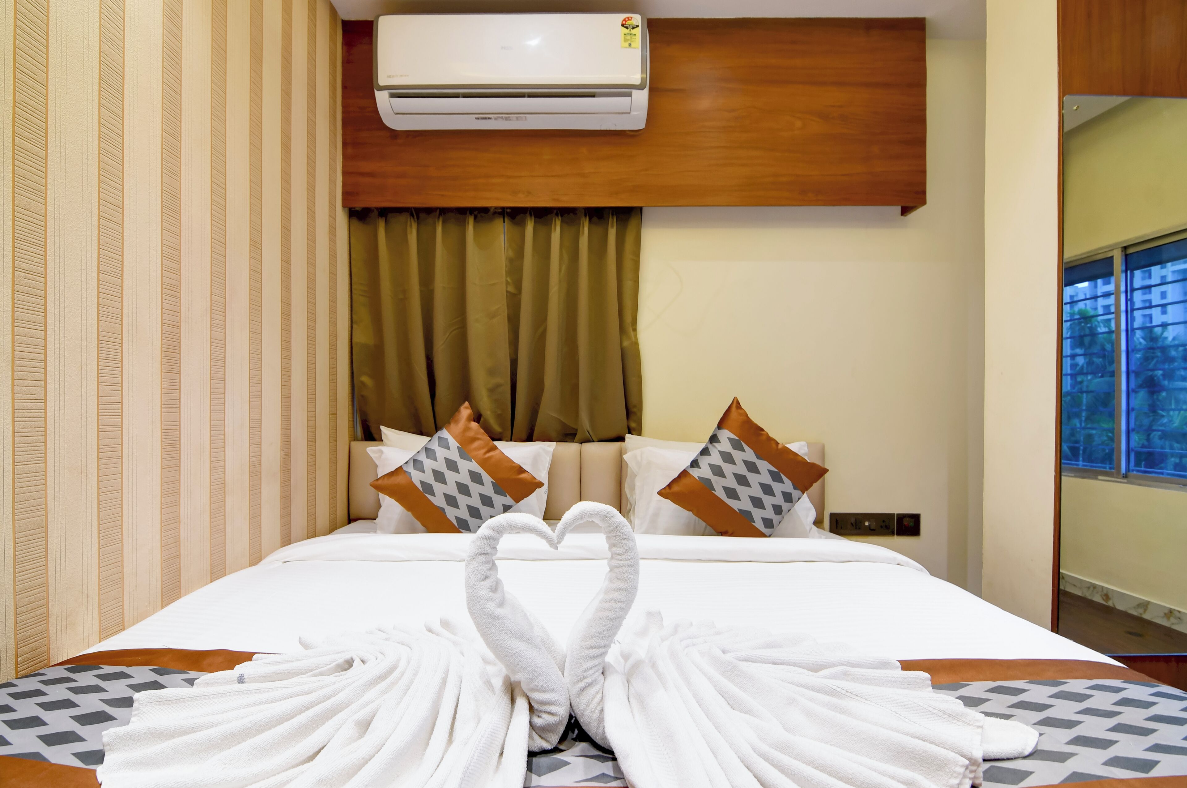 A hotel room with a bed, a wall-mounted air conditioner, and a window with a view.