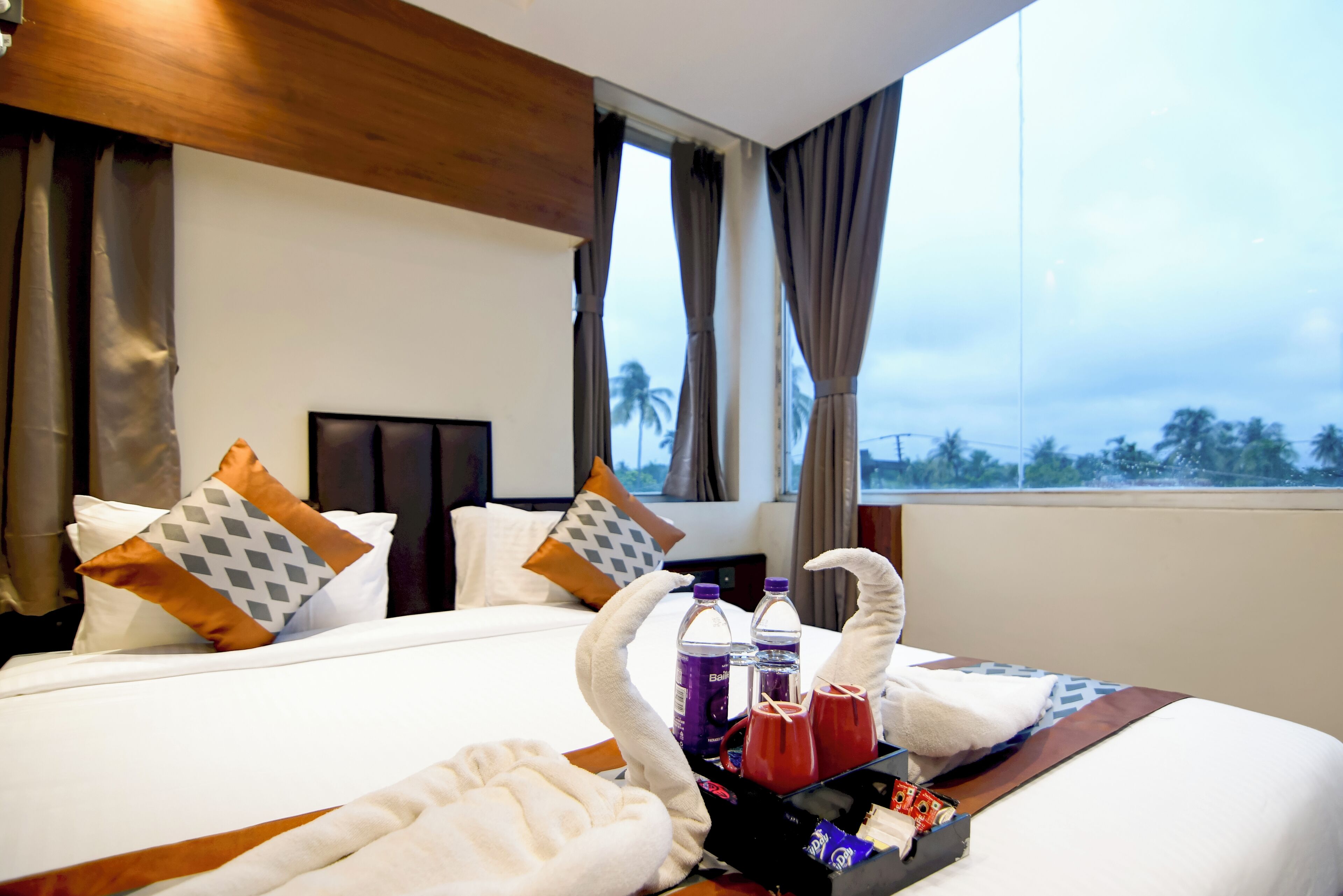 A hotel room with a bed, pillows, a tray with towels, bottles, and a box of chocolates.