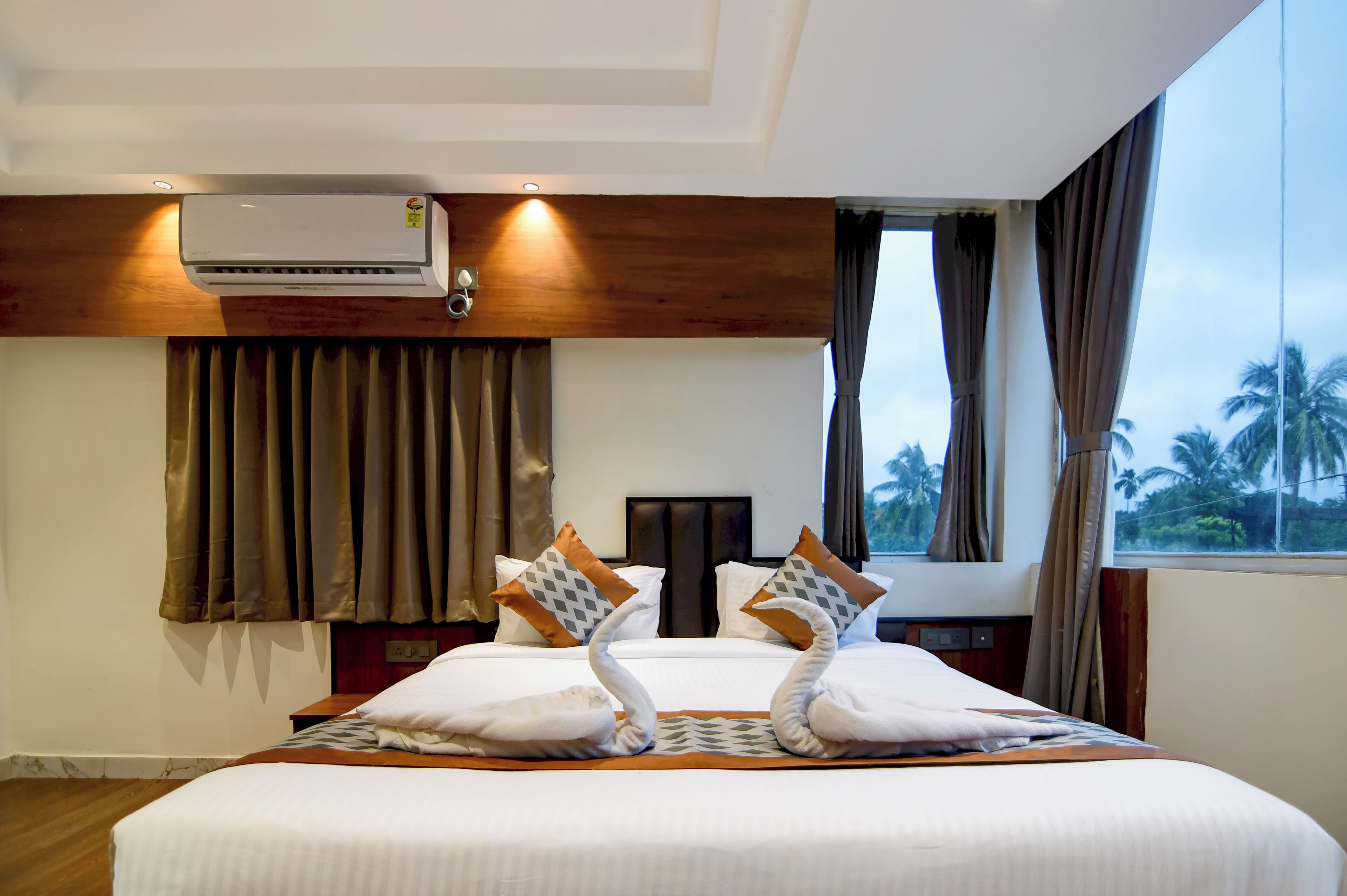 A hotel room with a bed, curtains, an air conditioning unit, and a view of palm trees.