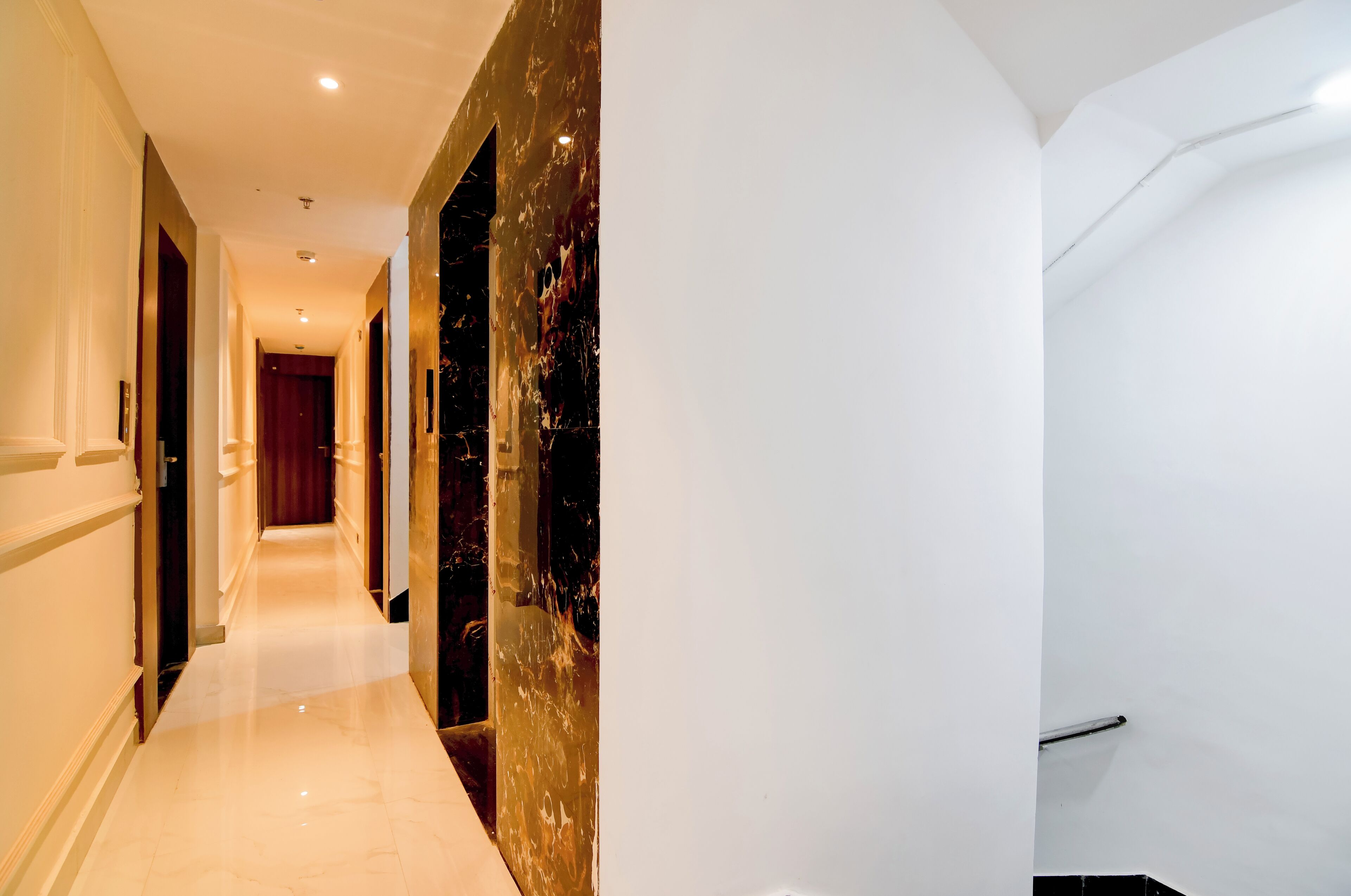 Un pasillo de hotel con suelo de mármol, una puerta roja al final y una pared con textura.