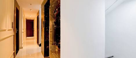 A hotel corridor with a marble floor, a red door at the end, and a wall with a textured pattern.