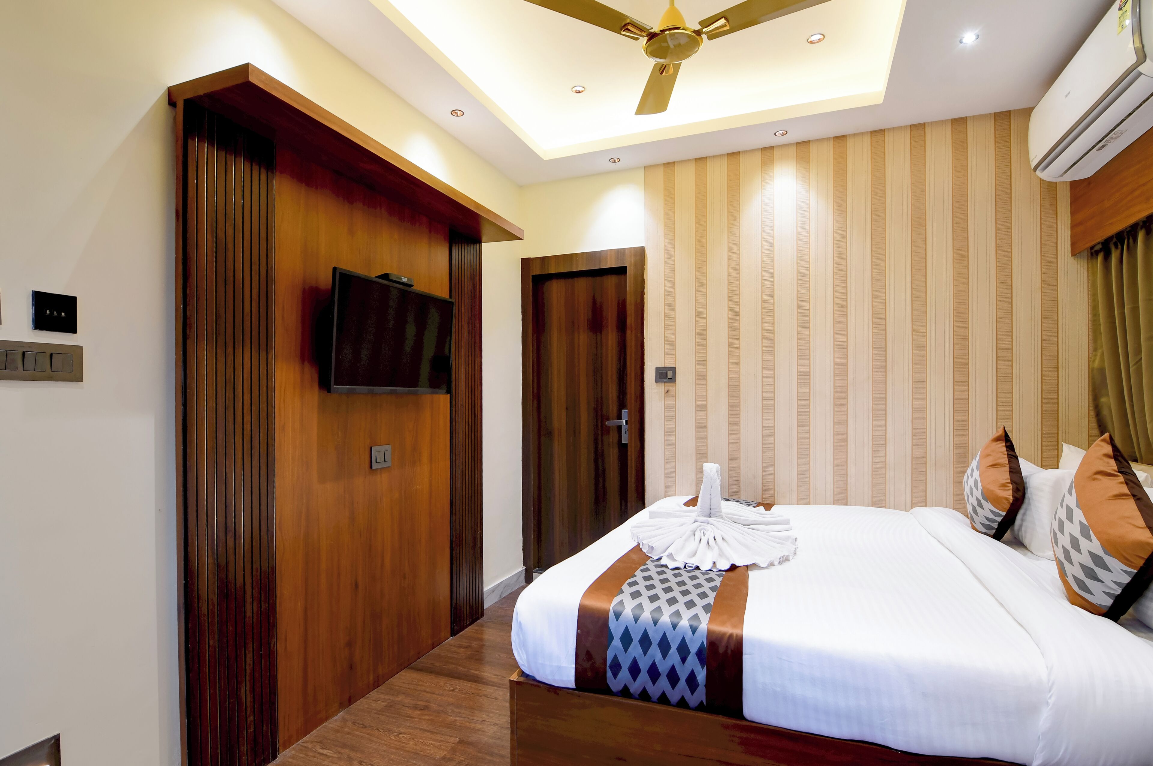 A hotel room with a bed, a television, a ceiling fan, and a door.