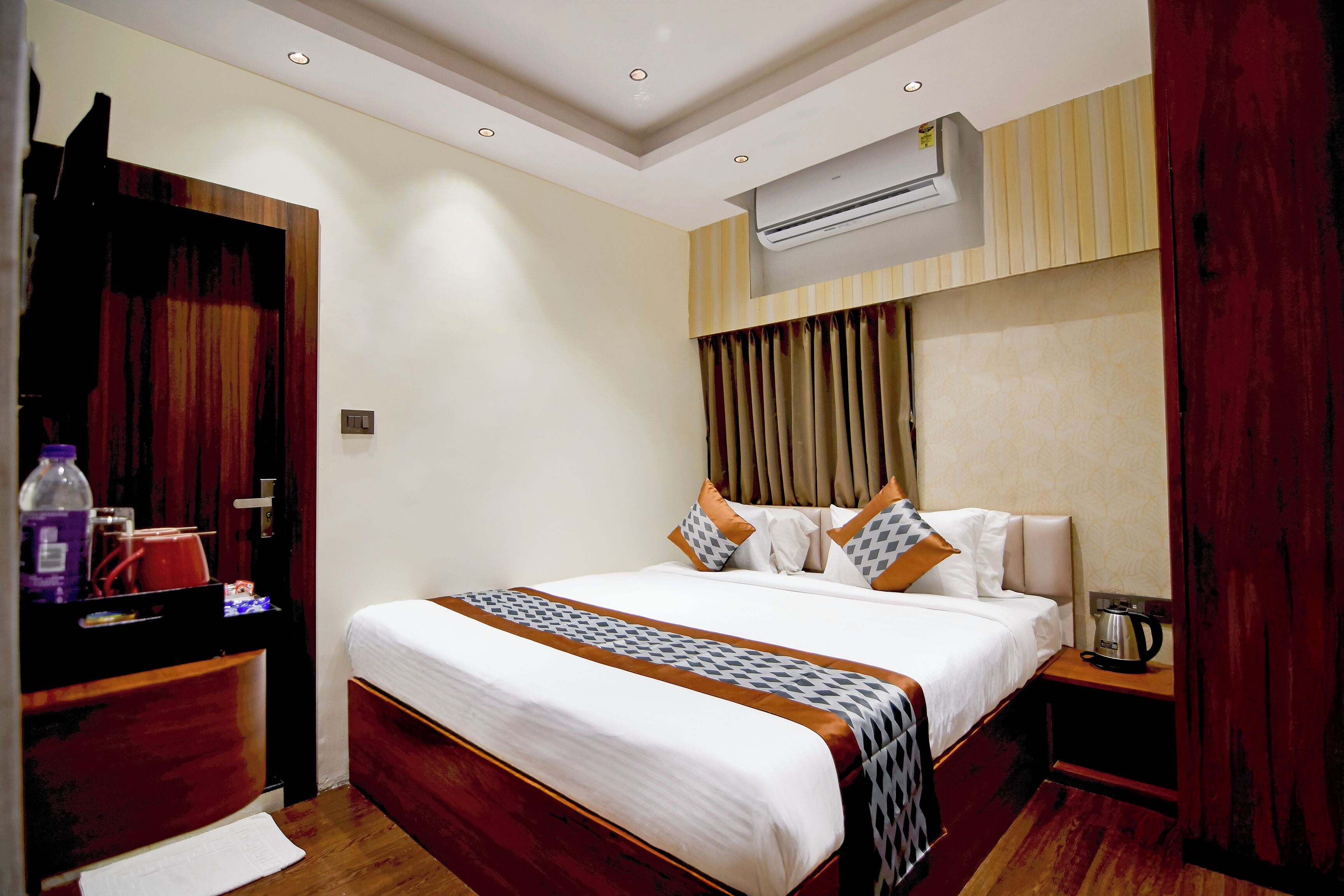 A hotel room with a bed, a bedside table, an air conditioning unit, and a wardrobe.