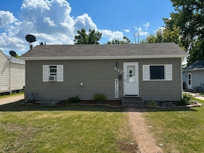 A single-story house with a white door and shutters, a satellite dish, and a welcome sign. - Perfect 2-bedroom house with AC in welcoming East Grand Forks (East Grand Forks)