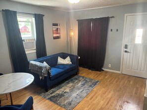 A room with a blue sofa, a small round table, a patterned rug, and a door.