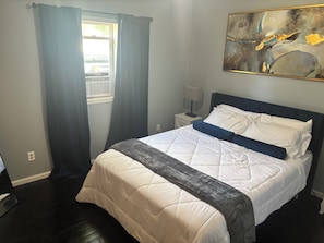 A bedroom with a bed, a nightstand, a lamp, and a painting on the wall. - Perfect 2-bedroom house with AC in welcoming East Grand Forks (East Grand Forks)