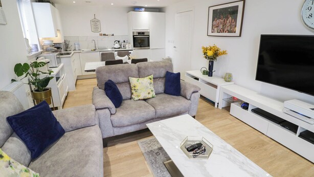 A modern living room with a grey sofa set, a coffee table, and a flat-screen TV. - 4 Goldcrest Close (Daventry)