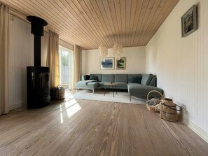 Ein modernes Wohnzimmer mit einer Eckcouch, einem schwarzen Kaminofen und einem großen Fenster mit Vorhängen.