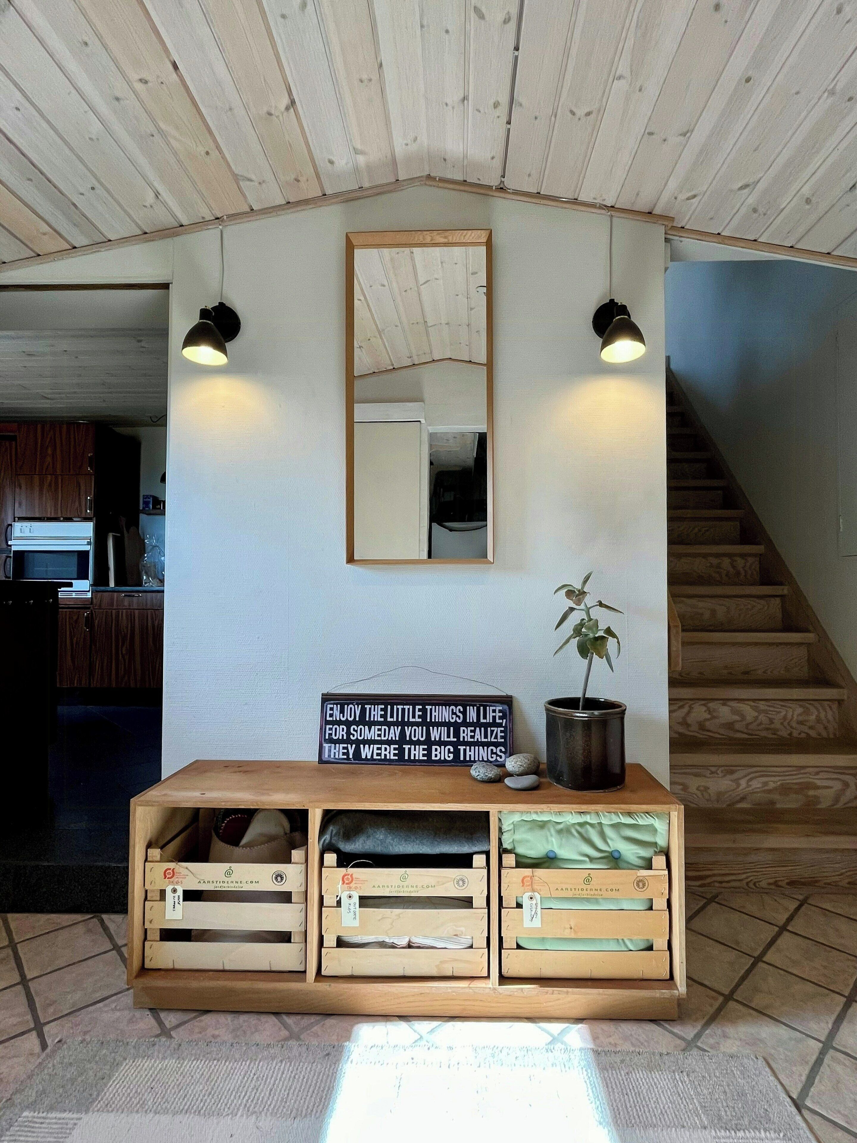 A room with a wooden ceiling, a mirror, a sign with a motivational quote, a potted plant, and a wooden bench with storage drawers.