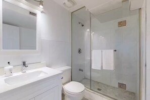 Et stilfuldt badeværelse med en glas brusekabine, en hvid vask og et toilet.