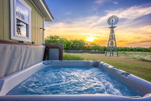 Een hottub met een houten terras, een windmolen op de achtergrond en een zonsondergang.