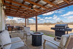 Een terras buiten met een barbecue, zitplaatsen en een vuurkorf.