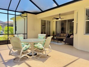 Eine sonnendurchflutete Terrasse mit Glasveranda, einem runden Tisch mit Stühlen, einer Couch und einem Deckenventilator.