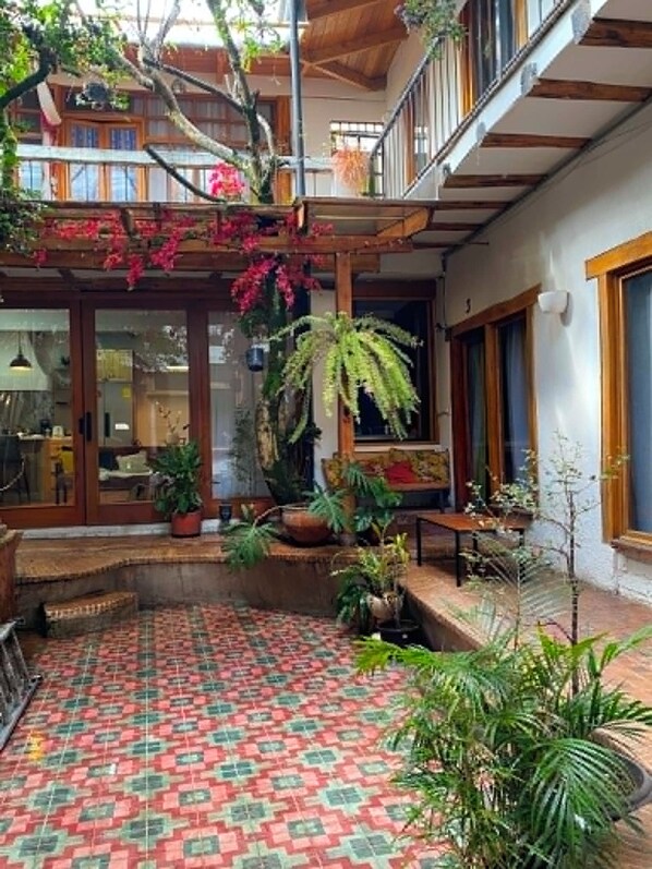 Une cour spacieuse avec un sol carrelé, entourée de plantes en pot et agrémentée d’un escalier en bois.