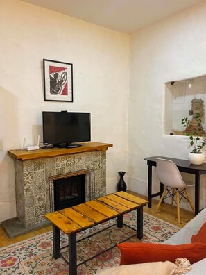 A living room with a fireplace, a television on a stand, a bench, a chair, and a window with a statue. - Lovely bachelor in Cuenca down-town (Cuenca)