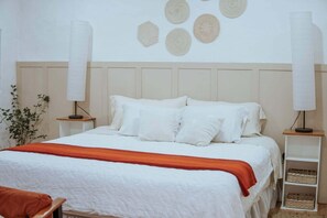 A neatly made bed with white linens and a red blanket, flanked by two bedside tables with lamps, in a room with a plain wall and a plant. - Lovely bachelor in Cuenca down-town (Cuenca)